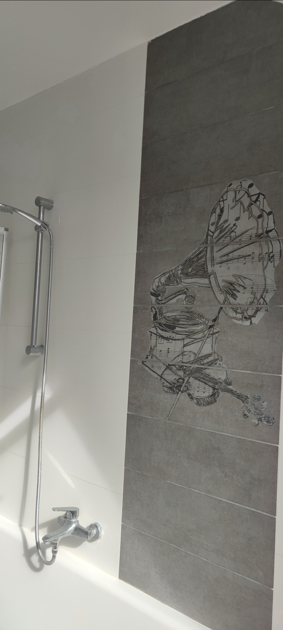 Biało-szara łazienka z prysznicem i baterią, ściana wyłożona płytkami z rysunkiem gramofonu i skrzypiec w stylu szkicu.