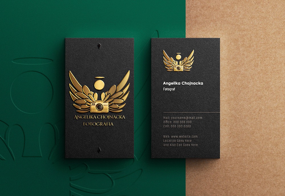 Dwie czarne wizytówki z tłoczonym złotym logo: aparat fotograficzny ze skrzydłami i aureolą, nazwa firmy Angelika Chojnacka Fotografia oraz dane kontaktowe na drugiej wizytówce, na tle zielonym...