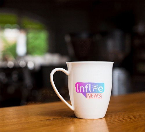 Biały kubek z nadrukowanym logo 'Influe NEWS' na drewnianym blacie, z rozmytym tłem kawiarnianym.