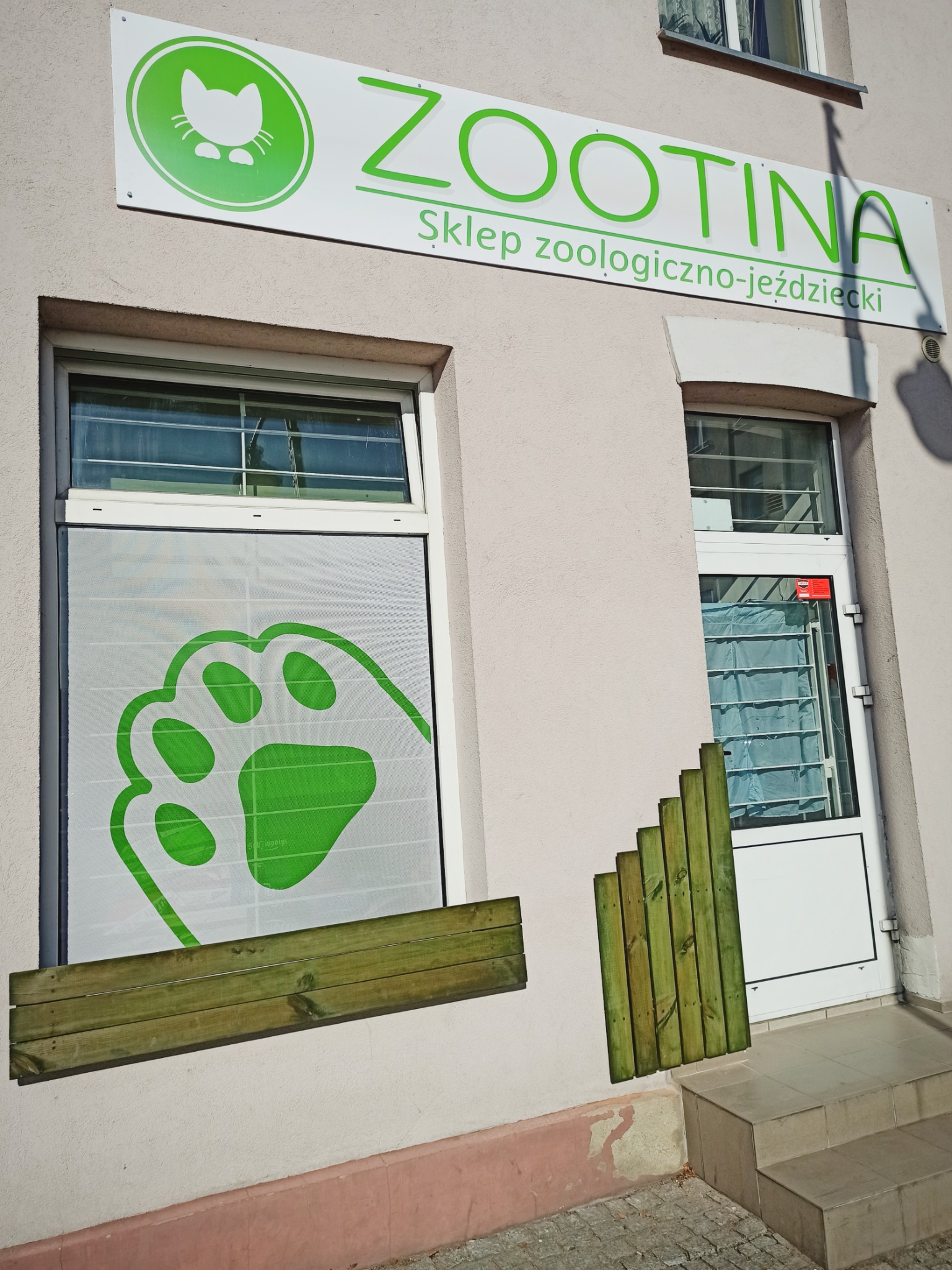 Fasada sklepu zoologiczno-jeździeckiego Zootina z zielonym logotypem kota i odciskiem łapy na oknie.