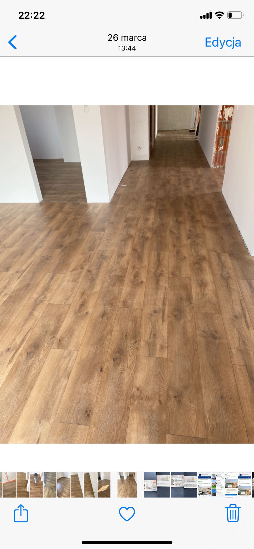 Ułożona podłoga z paneli imitujących drewno w jasnym odcieniu, widok na korytarz w trakcie prac wykończeniowych, białe ściany i filary, w tle surowy stan pomieszczenia.