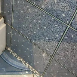 Szczegółowe ujęcie niebiesko-białych płytek mozaikowych na ścianie i podłodze w łazience, z widocznymi fugami i odblaskami światła.