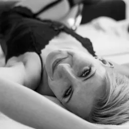 Portret kobiety leżącej na plecach w bieliźnie i pończochach kabaretkach, uśmiechająca się do kamery, czarno-białe zdjęcie z bliska.