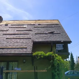 Częściowo zdjęte dachówki i widoczne łaty na dachu domu jednorodzinnego podczas remontu, rusztowanie przy ścianie, bluszcz na elewacji.