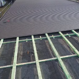 Montaż blachy trapezowej na dachu z widoczną konstrukcją drewnianą i narzędziami dekarskimi.