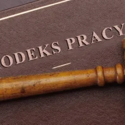 Drewniany młotek sędziowski leżący na brązowej książce z napisem 'Kodeks Pracy'.