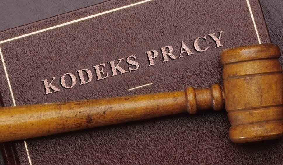 Drewniany młotek sędziowski leżący na brązowej książce z napisem 'Kodeks Pracy'.