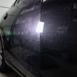 Część karoserii ciemnego samochodu, po lewej z widocznymi zarysowaniami i refleksami światła, po prawej po polerowaniu, z efektem głębi lakieru.