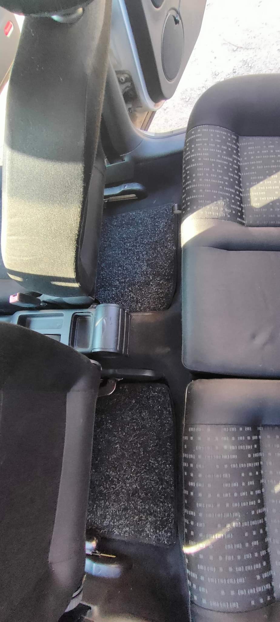 Wnętrze samochodu z widocznymi czarnymi fotelami z jasnym wzorem, dywanikami pod nogami oraz elementami plastikowymi deski rozdzielczej i progów.