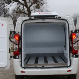FORMAT 74 Maciej Dranicki - Tył białego furgonetki chłodni z otwartymi drzwiami, widoczna pusta, czysta przestrzeń ładunkowa z aluminiową podłogą i agregatem chłodniczym na dachu.