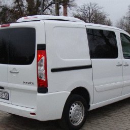 FORMAT 74 Maciej Dranicki - Biały bus Toyota ProAce z chłodnią na dachu, widok z tyłu, zaparkowany na brukowanym placu przy drodze.