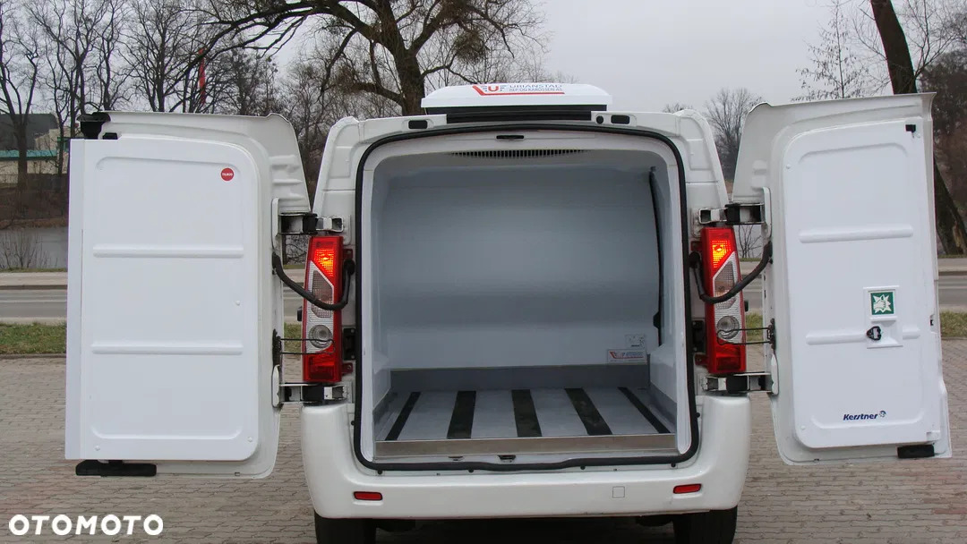 Tył białego furgonetki chłodni z otwartymi drzwiami, widoczna pusta, czysta przestrzeń ładunkowa z aluminiową podłogą i agregatem chłodniczym na dachu.