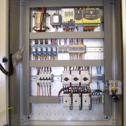 PGiG sp. z o.o. - Otwarta szafa sterownicza z widocznymi elementami elektrycznymi, okablowaniem i zabezpieczeniami, zainstalowanymi na szynach DIN, z żółto-zielonym przewodem uziemiającym w lewym dolnym rogu.