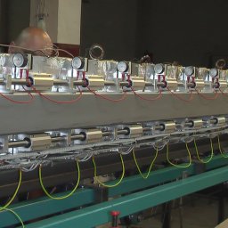 PGiG sp. z o.o. - Szczegółowe ujęcie fragmentu maszyny przemysłowej z rzędem cylindrów pneumatycznych, przewodami i manometrami, widok z boku z fragmentem głowy majsterkowicza w tle.