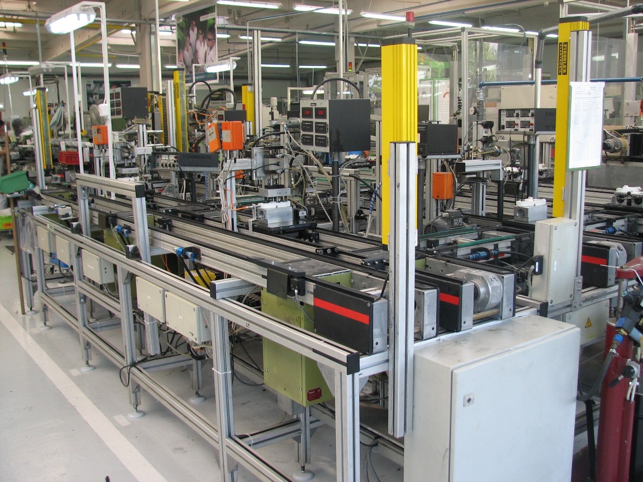 Automatyczna linia produkcyjna w hali fabrycznej z żółtymi elementami konstrukcyjnymi i systemem przenośników taśmowych.