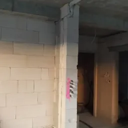 Surowy stan budynku w trakcie prac: widoczne kable elektryczne prowadzone po suficie i wzdłuż ściany z betonu komórkowego, z zaznaczonym na różowo miejscem na gniazdka.