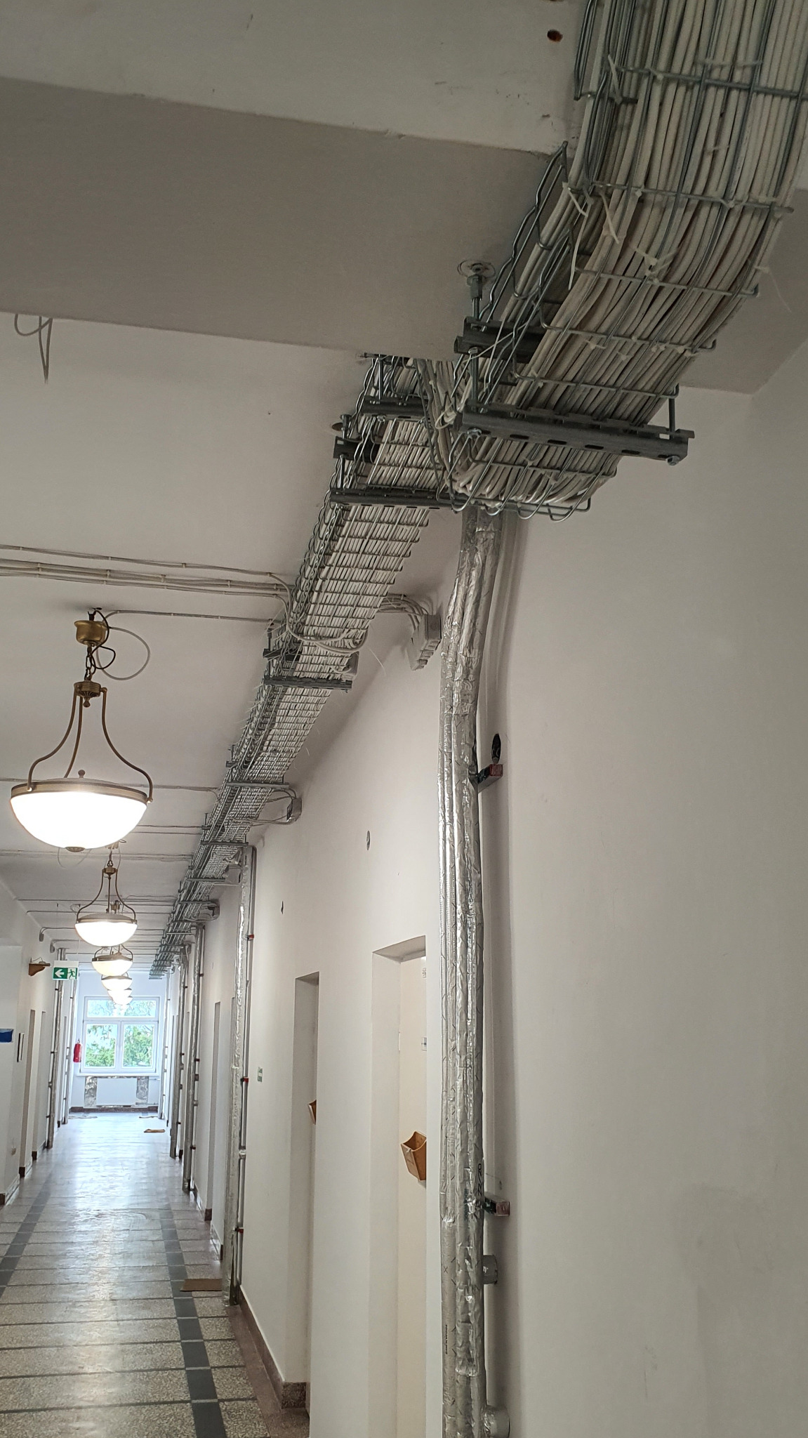 Rozprowadzenie instalacji elektrycznej w korytarzu dużego obiektu mieszkalnego, przed zabudową sufitu.