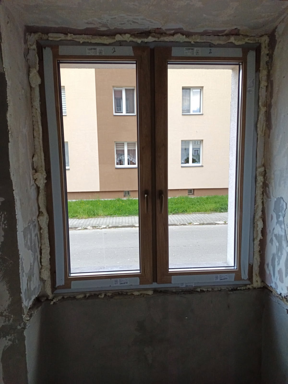 Montaż okna PCV w Libiążu. Profil Moderntherm w kolorze Turner oak, widok na zewnątrz. Pianka montażowa wokół ramy okiennej. Parapet MDF w kolorze Turner oak.