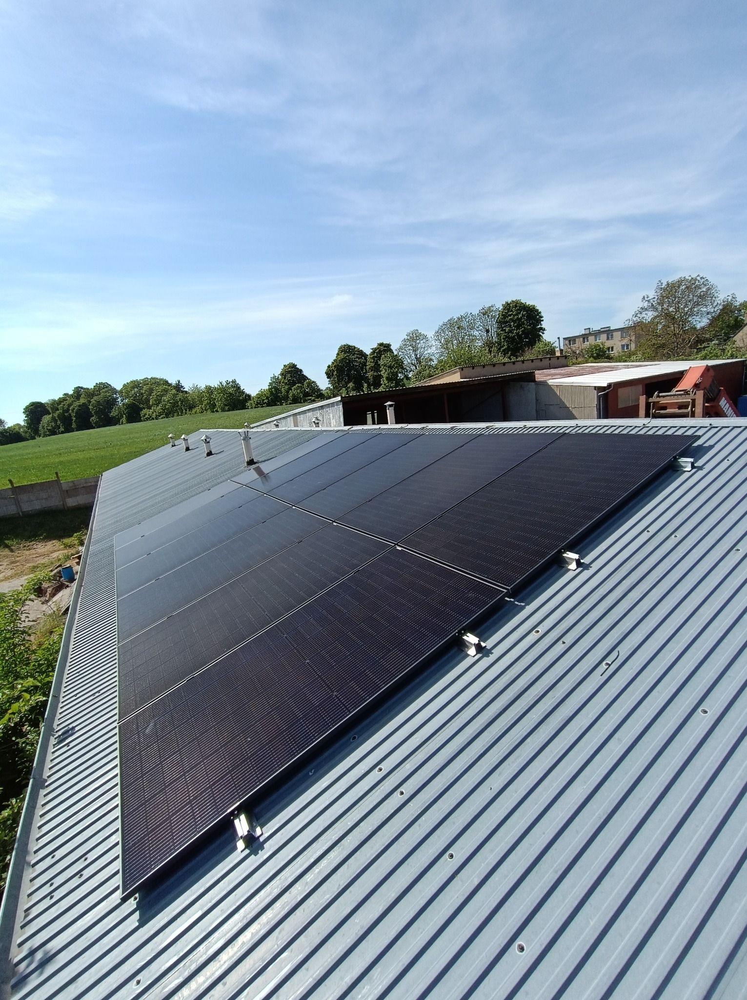 Panele słoneczne zamontowane na blaszanym dachu budynku gospodarczego, widok z góry na instalację w słoneczny dzień.