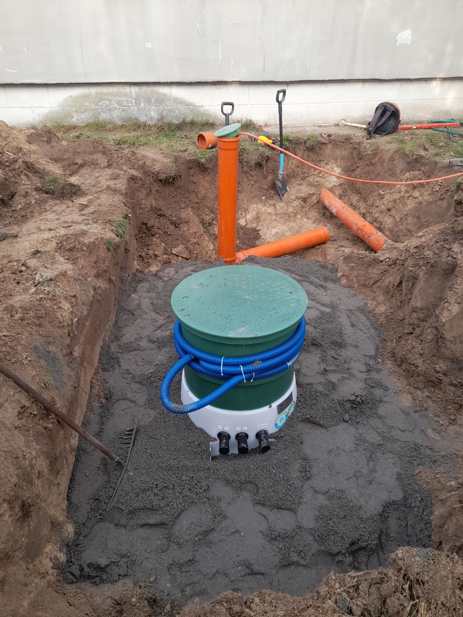 Płaski zbiornik oczyszczalni ścieków, zabezpieczony w wykopie z wysokim poziomem wód gruntowych, otoczony szarym podsypem stabilizującym.