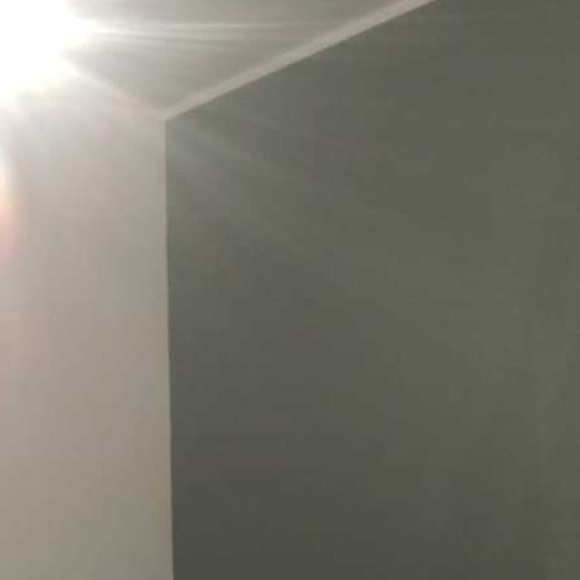 Świeżo pomalowany narożnik pokoju, gdzie jedna ściana jest biała, a druga ma odcień szarości, widoczne delikatne smugi światła.
