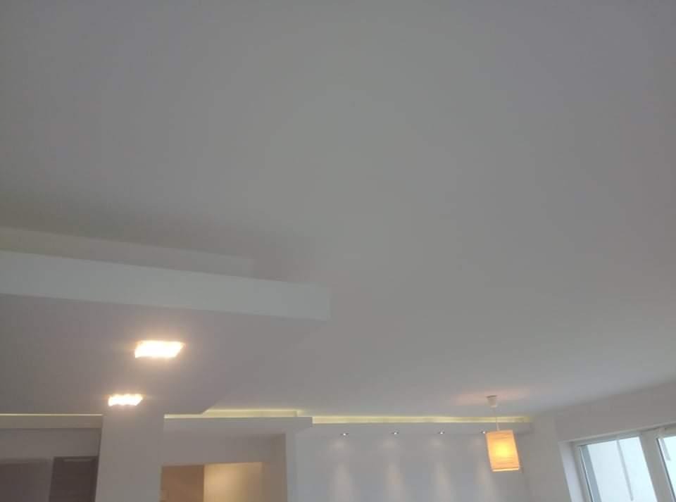 Gładki, biały sufit po renowacji z wbudowanym oświetleniem punktowym i dekoracyjnym paskiem LED, widok z dołu.