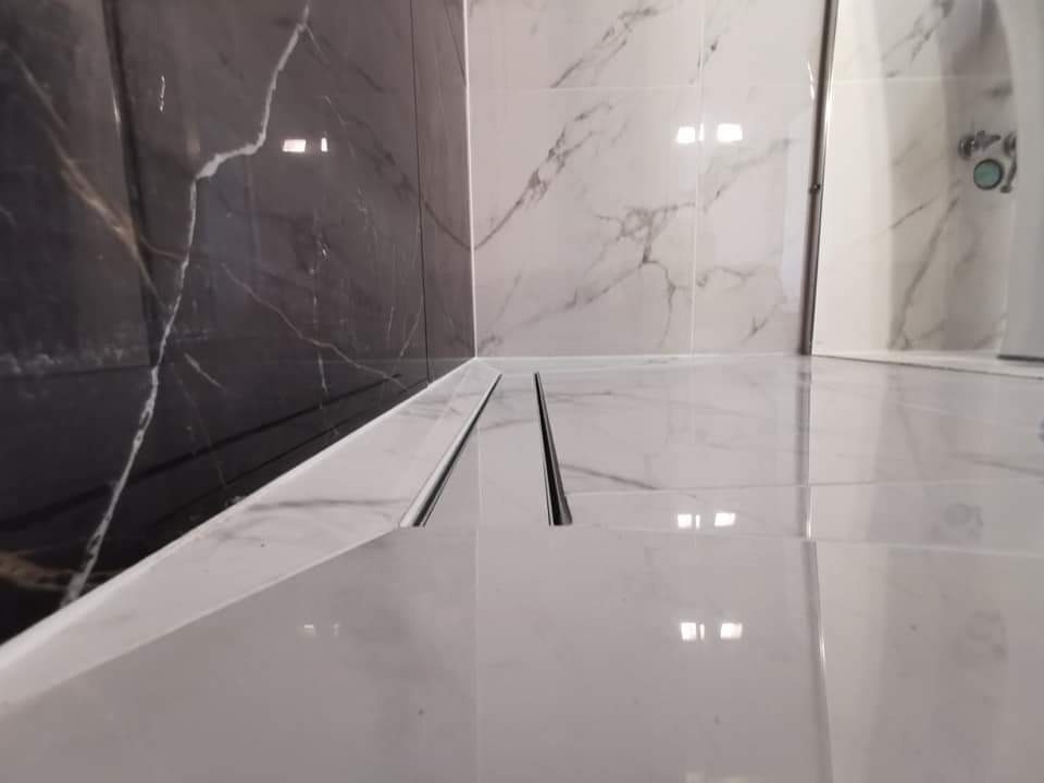 Nowoczesna łazienka z czarno-białymi marmurowymi płytkami, widoczny odpływ liniowy w podłodze i fragment kabiny prysznicowej.