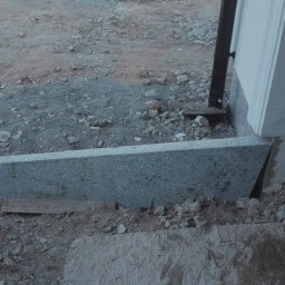 ggworkbruk - Granitowy element schodowy w trakcie montażu, widoczny fragment ściany budynku, gruz i drewniane podpórki.