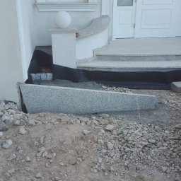 ggworkbruk - Montaż granitowej obudowy schodów wejściowych do domu, widoczna czarna folia izolacyjna, gruz i zaparkowany samochód.