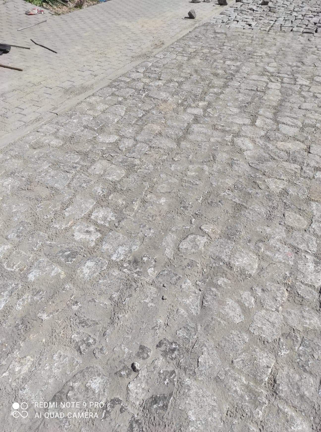 Fragment powierzchni z szarej kostki granitowej w trakcie układania, widoczne szczeliny wypełnione piaskiem i niedokończony fragment obok.