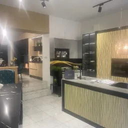 Salon ekspozycyjny z nowoczesną zabudową kuchenną w odcieniach drewna i szarości, z wyspą kuchenną z blatem z szarego spieku i dekoracyjnym oświetleniem wiszącym.