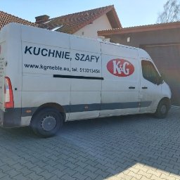 K&G MEBLE KINGA GNYLA - Biały samochód dostawczy z napisem 'Kuchnie, Szafy' oraz logo firmy K&G, zaparkowany na brukowanej nawierzchni przed domem z garażem.