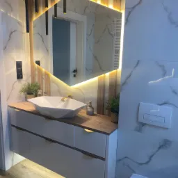 Nowoczesna łazienka z umywalką w kształcie diamentu, podświetlanym lustrem o heksagonalnym kształcie i drewnianymi akcentami na ścianie, marmurowe płytki.