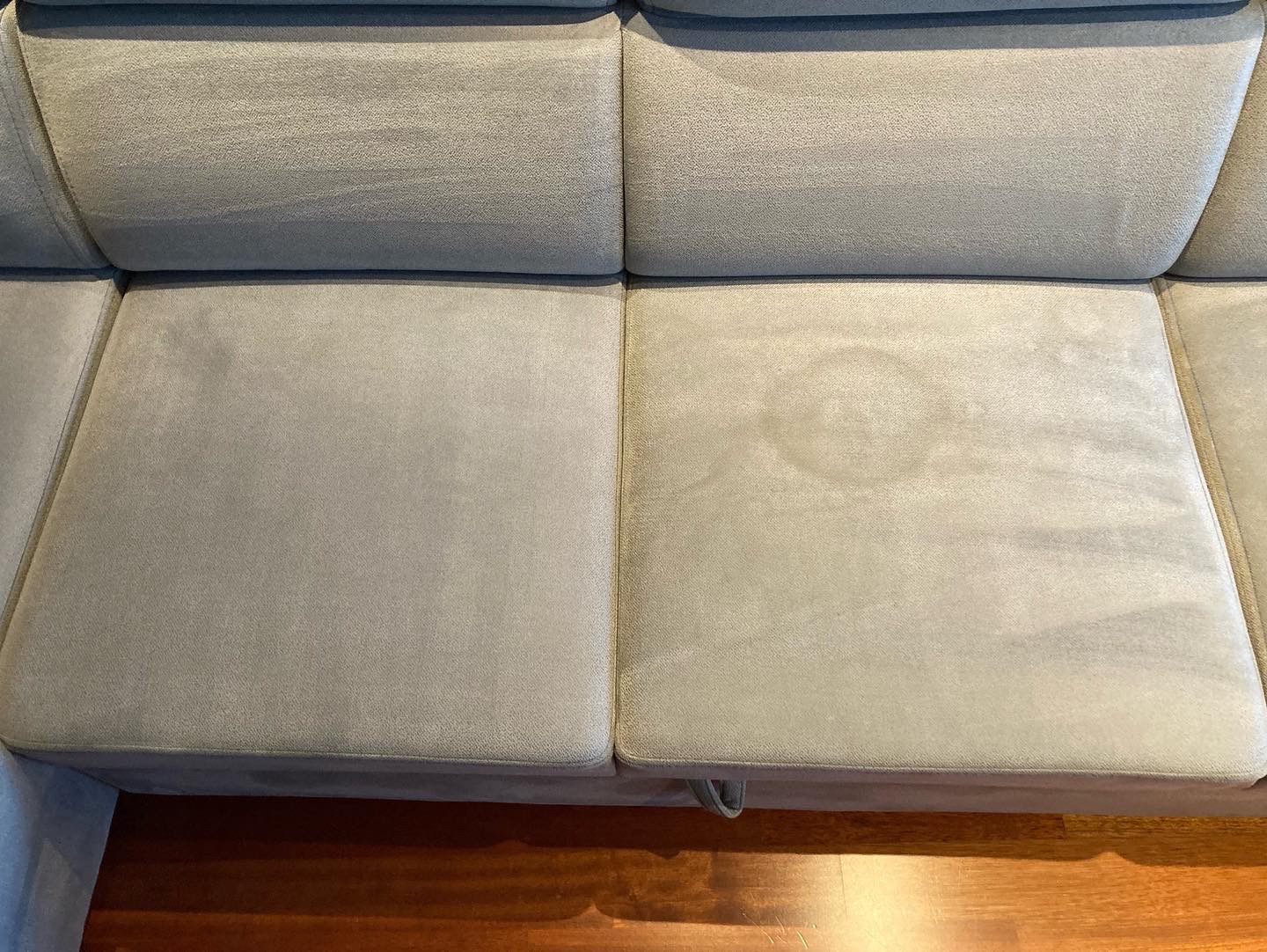 Porównanie siedzisk kanapy przed i po czyszczeniu: po lewej stronie czyste, po prawej widoczna okrągła plama na szarym welurze.