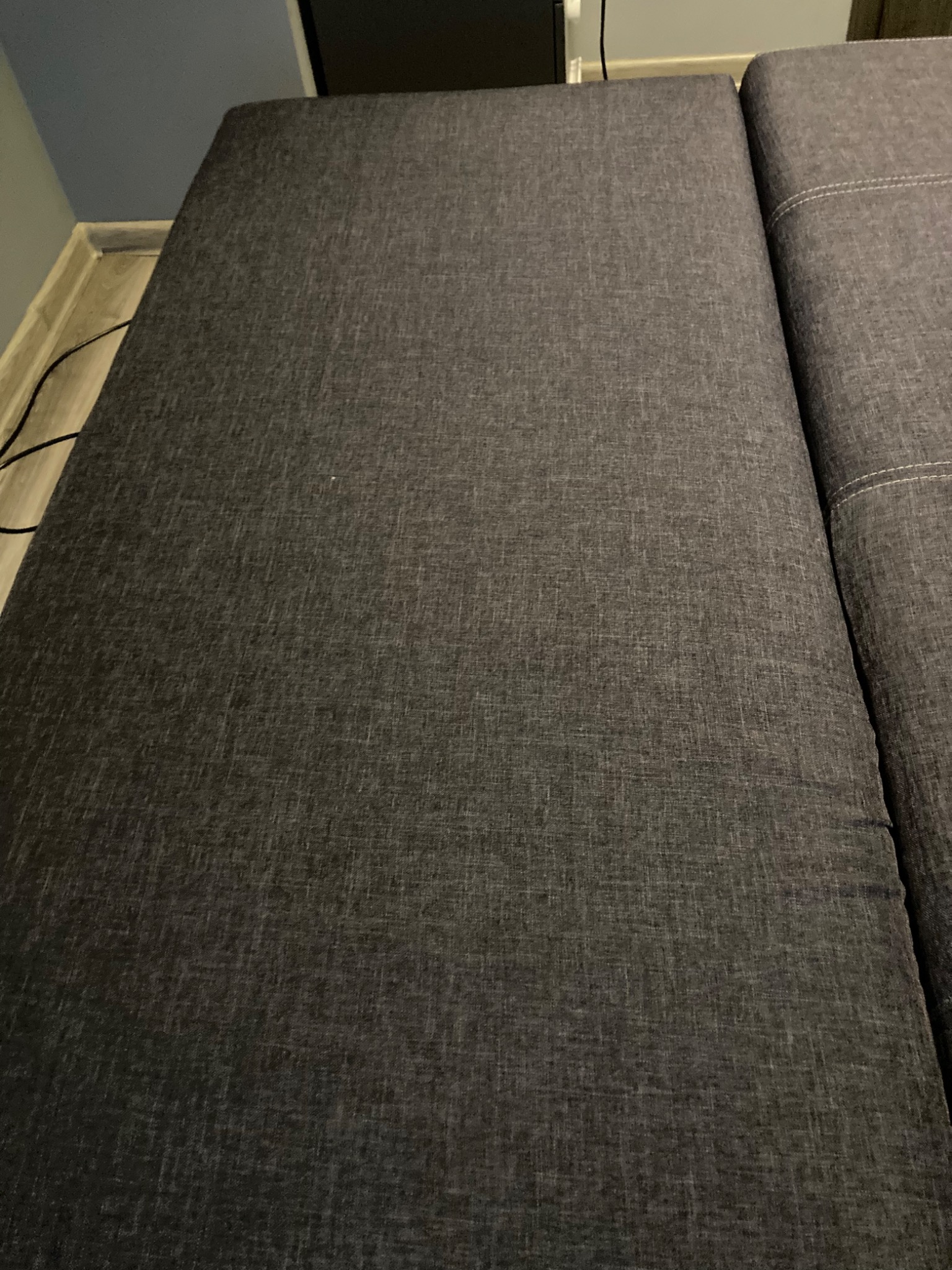 Fragment ciemnoszarej kanapy z widocznym szwem, sfotografowany z góry, ukazujący fakturę materiału.