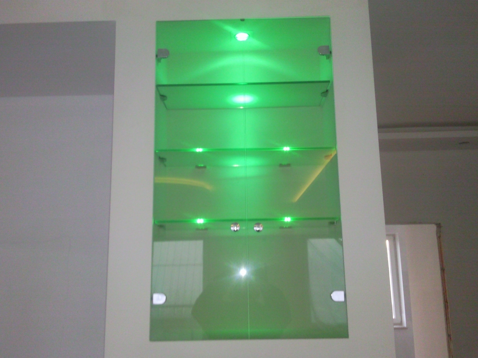 Szklana witryna z półkami podświetlonymi zielonymi diodami LED, zamontowana we wnęce ściany.