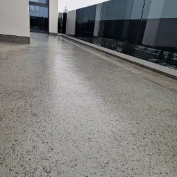 Polerowana, szara posadzka z mikrocementu na balkonie z nowoczesną szklaną balustradą, widok na zewnątrz w pochmurny dzień.