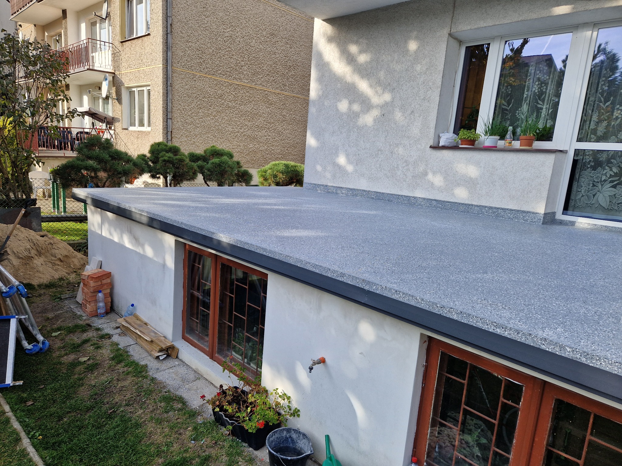 Szary taras z wykończeniem z żywicy epoksydowej, widok z góry na tle budynku mieszkalnego i zieleni.