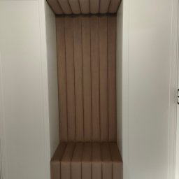 Marek Krajnik - Wnęka z siedziskiem i tapicerowanymi panelami ściennymi w odcieniach beżu, wkomponowana w białą zabudowę meblową. Nowoczesny design, pionowe przeszycia.