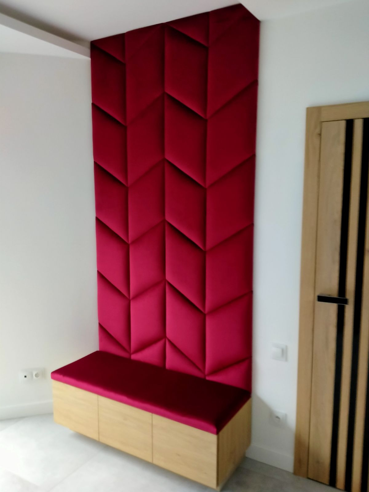 Panel ścienny z siedziskiem w kolorze fuksji, geometryczny wzór, wykonany na wymiar w Piastowie. Obok widoczna drewniana, nowoczesna stolarka drzwiowa.