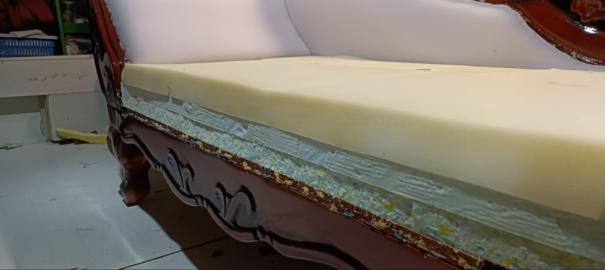 Rozłożona sofa z widocznymi warstwami wypełnienia: pianka, włóknina i sprężyny. Ciemne, zdobione drewniane elementy ramy. Etap prac renowacyjnych.