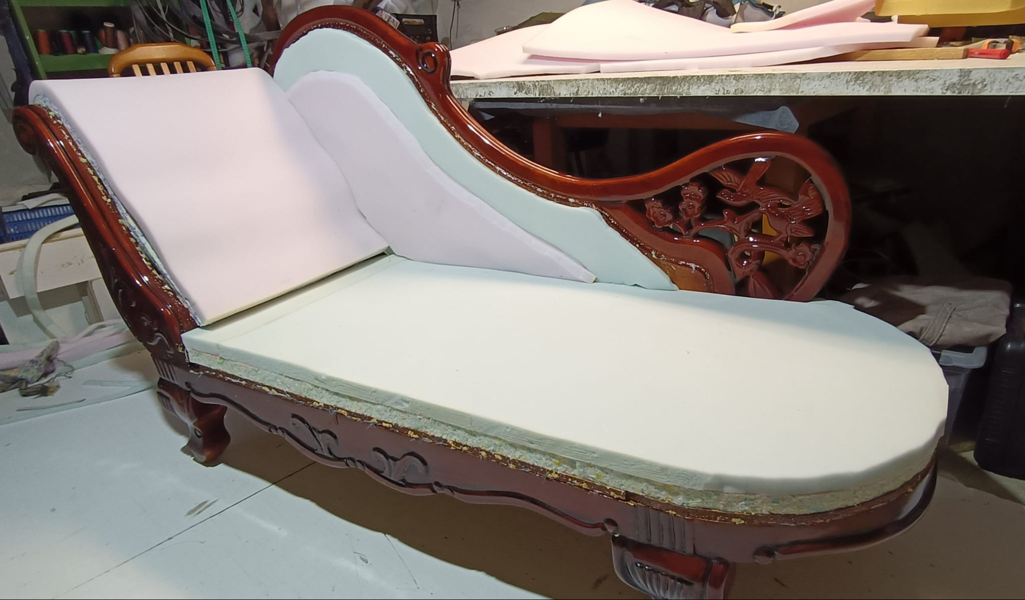 Antyczny szezlong z rzeźbioną ramą w trakcie renowacji. Widoczne warstwy pianki tapicerskiej, przygotowane do obicia materiałem. Detal rzemiosła.
