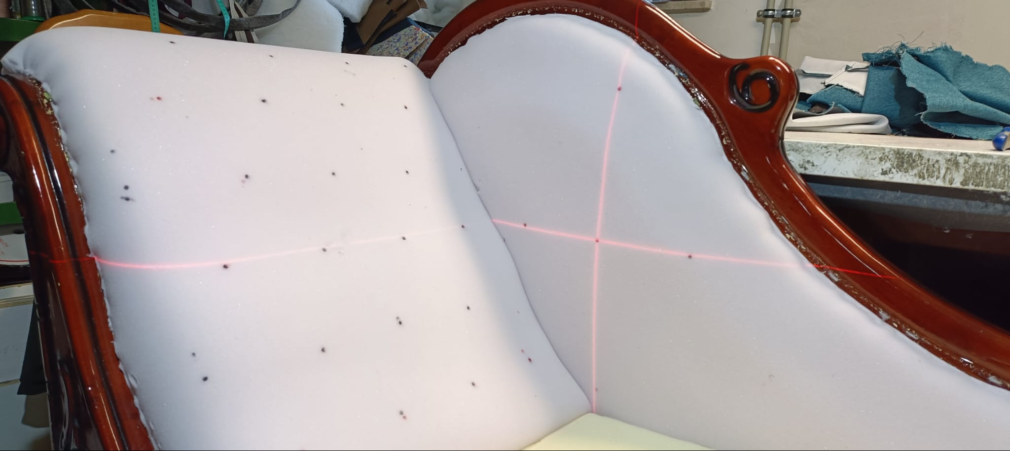 Tapicerowanie sofy w stylu retro. Biała pianka z zaznaczonymi punktami, czerwone linie lasera, drewniana rama w kolorze brązowym. Etap przygotowania do obicia.