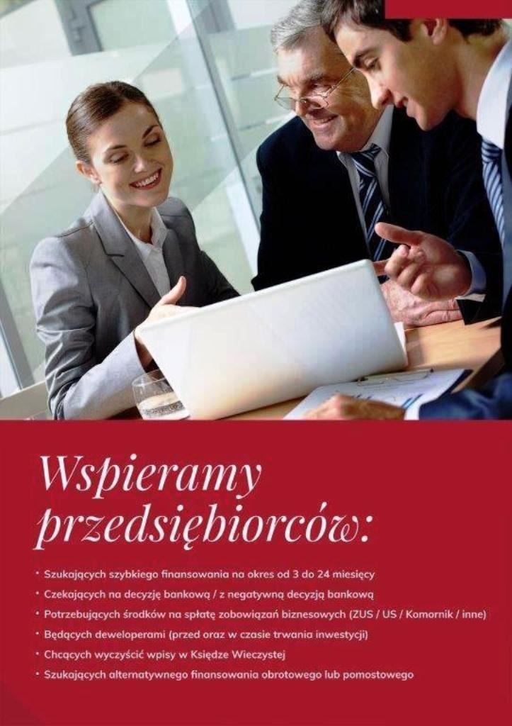 Trzy osoby w garniturach omawiają dokumenty na stole, z laptopem i szklanką wody, uśmiechnięta kobieta w szarym żakiecie wskazuje na ekran.