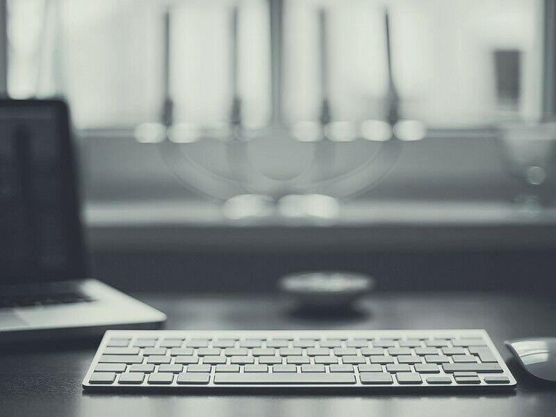 Minimalistyczne biurko z laptopem, klawiaturą i myszką na tle okna, utrzymane w monochromatycznej tonacji.