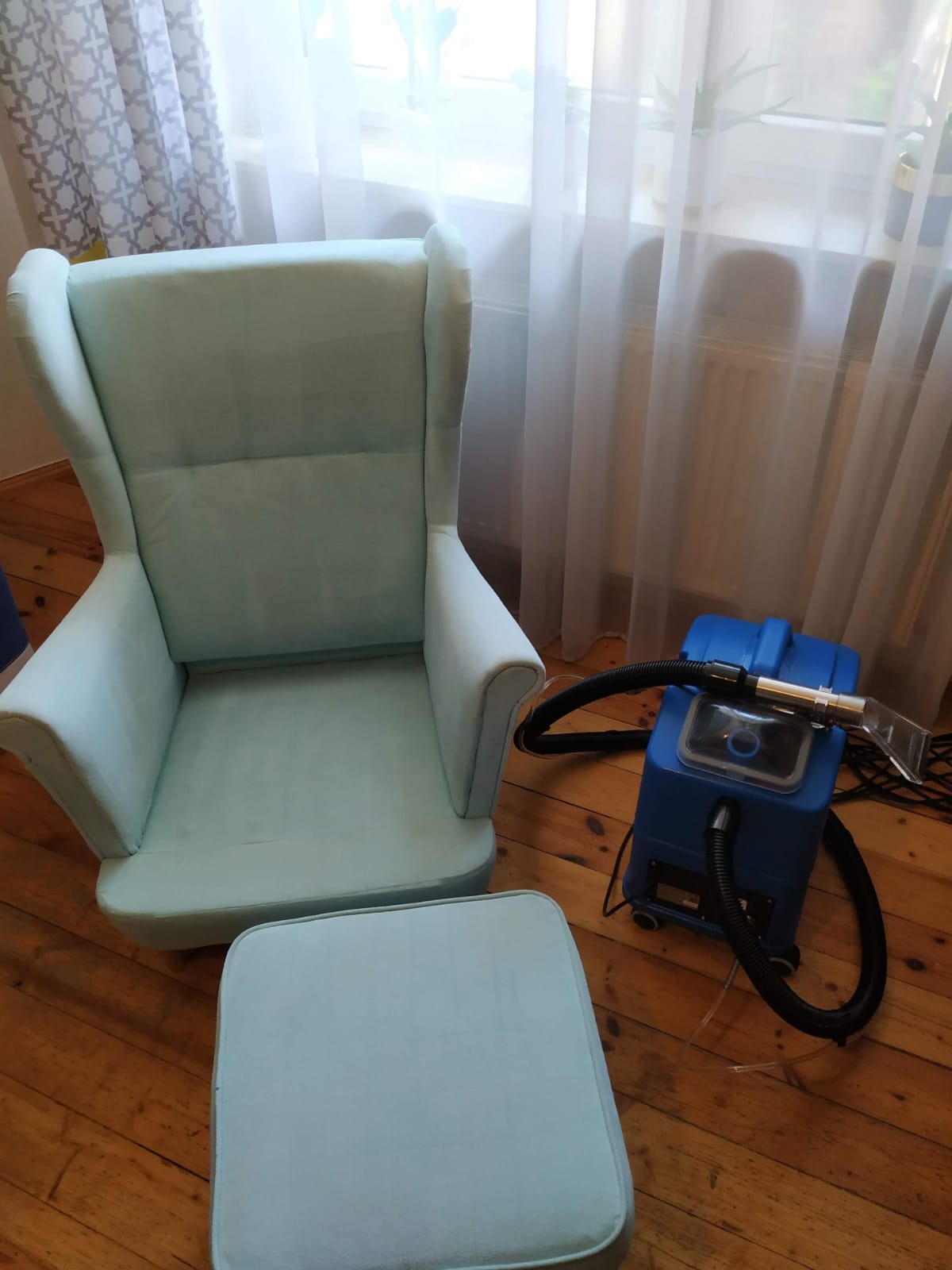 Jasnoniebieski fotel uszak i podnóżek obok profesjonalnego ekstraktora do czyszczenia tapicerki na drewnianej podłodze w jasnym wnętrzu.