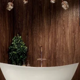 Nowoczesna łazienka z wolnostojącą białą wanną na tle drewnianej ściany, akcentowana miedzianą armaturą i szklanymi lampami wiszącymi oraz rośliną doniczkową.