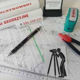 Szkic mapy geodezyjnej z naniesionymi pomiarami, otoczony narzędziami: ołówek automatyczny Rotring Tikky, cyrkiel z czerwoną końcówką, linijka, kątownik, pieczątka firmowa i rolki papieru...