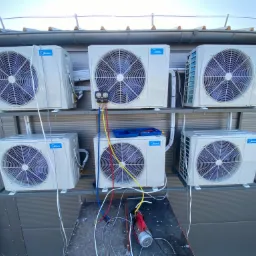 Sześć zewnętrznych jednostek klimatyzacji Midea zamontowanych na metalowych wspornikach na zewnątrz budynku, z widocznymi narzędziami serwisowymi podłączonymi do jednej z jednostek.