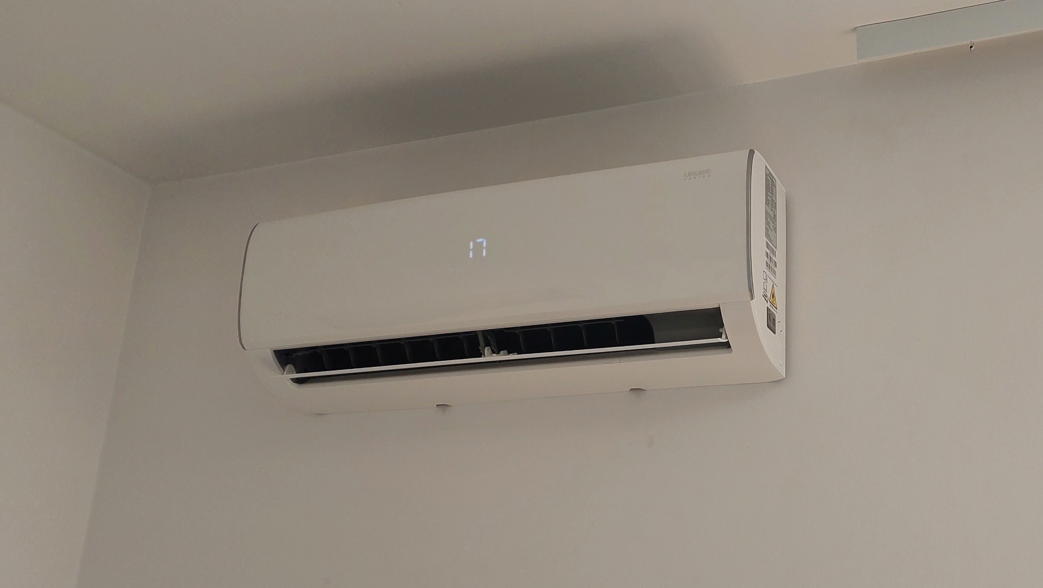 Biała klimatyzacja ścienna z wyświetlaczem temperatury ustawionym na 17 stopni Celsjusza, zamontowana na jasnej ścianie w pomieszczeniu.